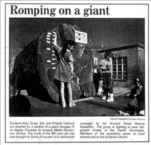 Newspaper clipping shows two children standing on a truck bed touching a giant log that has little signs pinned to its rings